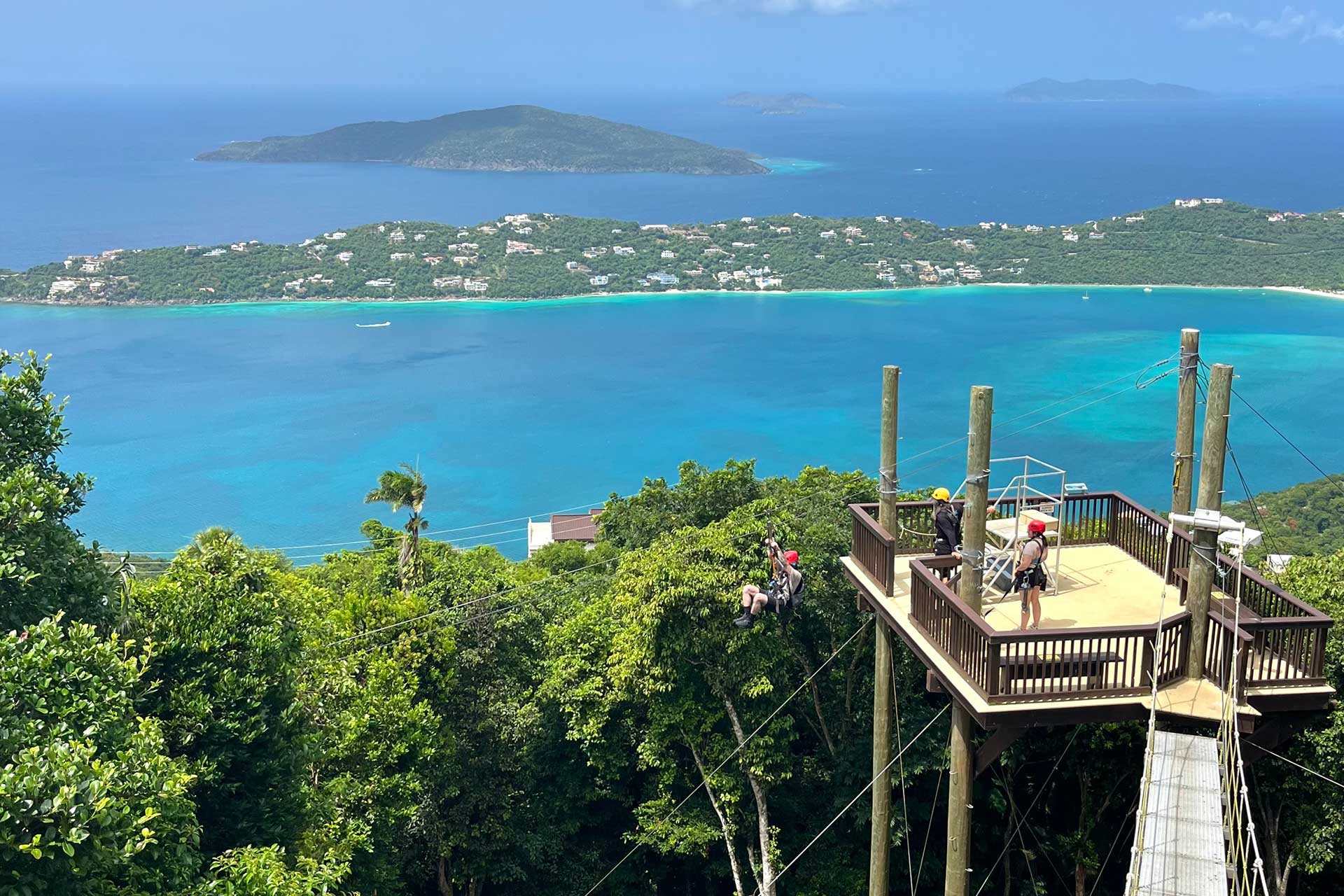 Guest ziplining through the rainforest. Backdrop includes views of Magens Bay and surrounding Caribbean islands.