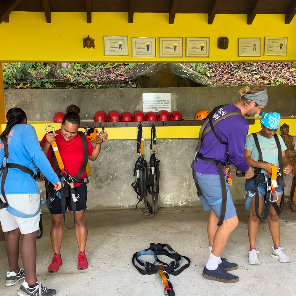 Zipline tour guides gearing guests in harnesses and helmets before zipping through the canopy.