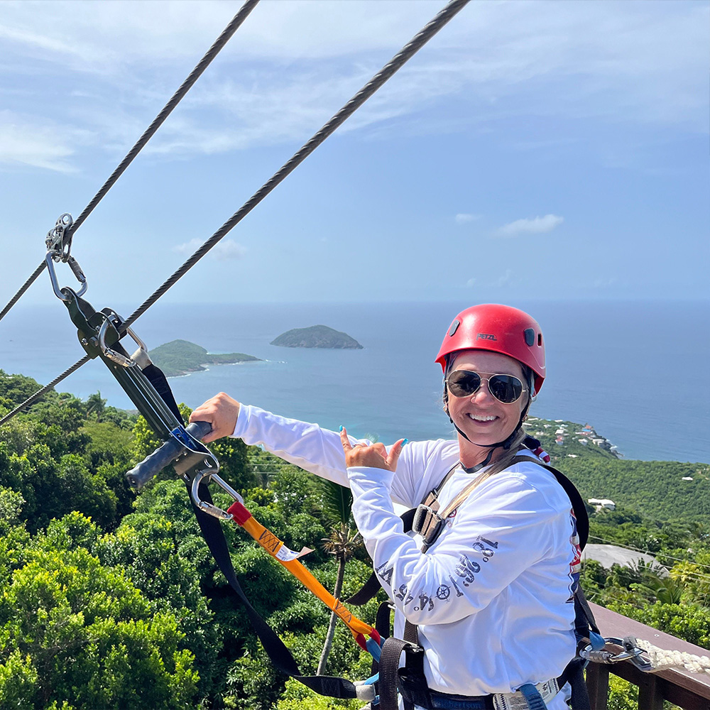 Guest on the 'Yo-Yo' zip smiling hooked up to zip the final zipline. Caribbean islands in sight.