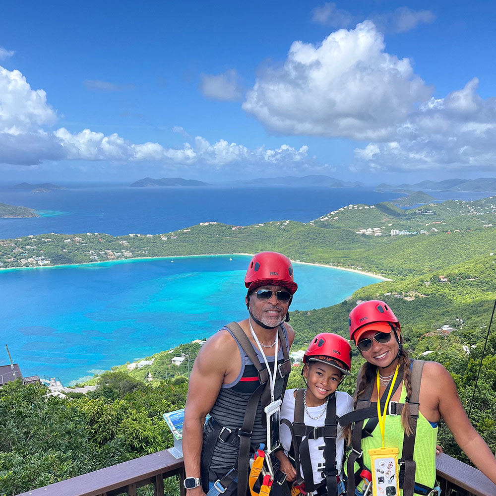 Family of three posed on a zipline platform with a clear shot of Magens Bay, the BVI, St. John and beyond.