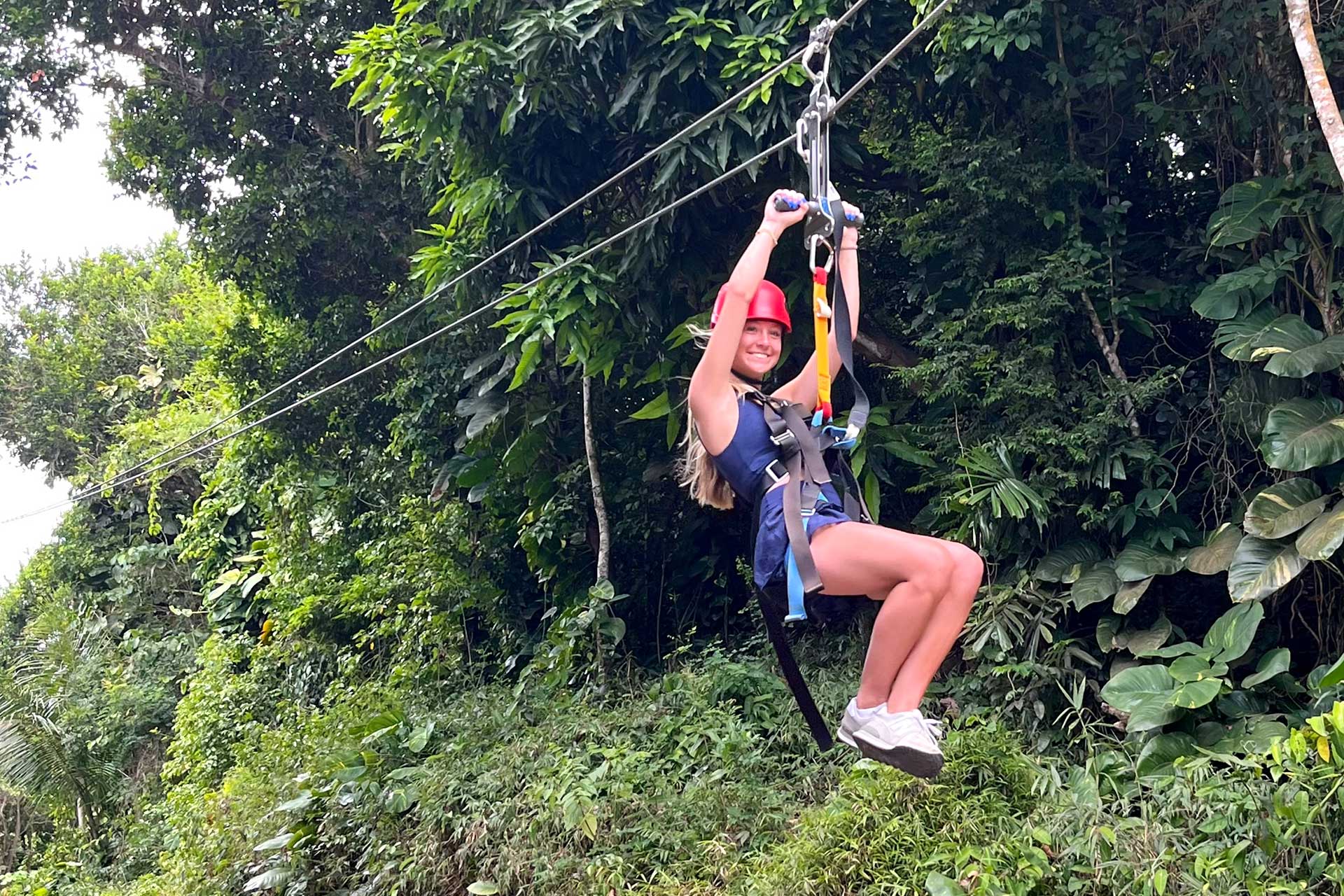 Woman smiling ziplining through the trees at Tree Limin' Extreme Zipline located in St. Thomas, USVI.
