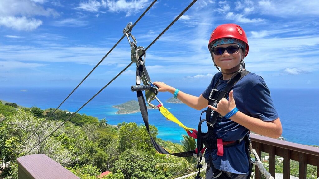 Child on take-off 6 posing smiling with the backdrop of the Caribbean islands and turquoise waters before going ziplining.