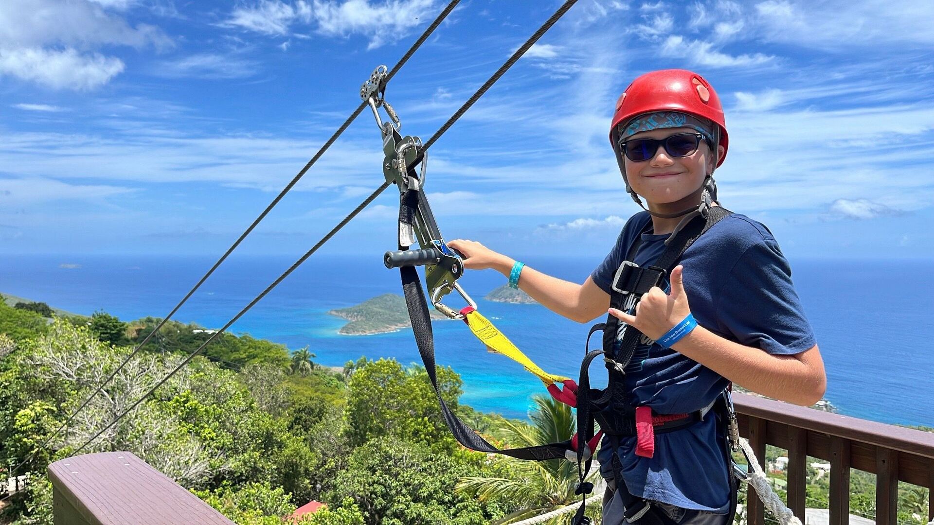 Child on take-off 6 posing smiling with the backdrop of the Caribbean islands and turquoise waters before going ziplining.
