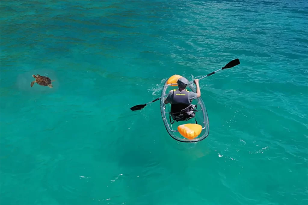 Clear bottom kayak with person kayaking next to a sea turtle in turquoise waters. St. Thomas activities that provide an all-inclusive vacation.