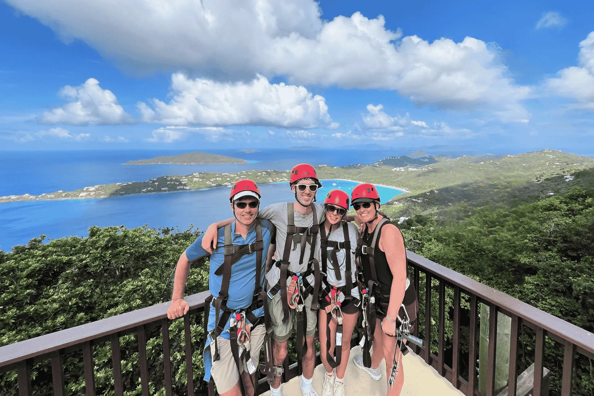 Family smiling in zipline gear with background of St. Thomas. Magens Bay views.